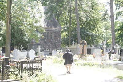 Widok na aleje prowadzącą przez cmentarz, otoczoną nagrobkami.
